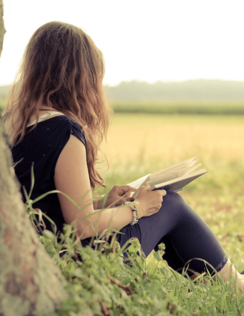 Woman reading book under tree in grassy field