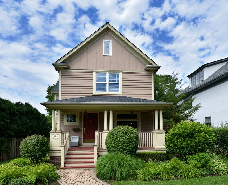 Tan two-story house with porch and shrubs
