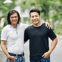Two men smiling outdoors, arm over shoulder